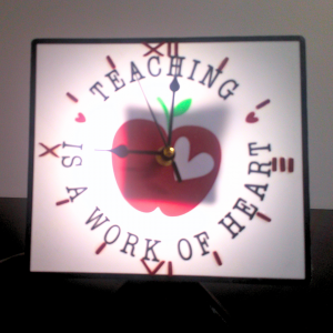 teacher's clock with a red apple, and it says "Teaching is a work of Heart" and lights up.